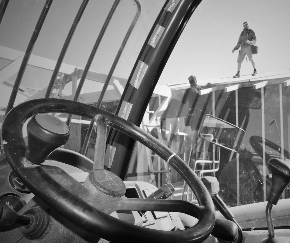 Poste de conduite d’un engin de chantier avec artisans travaillant sur une structure bois